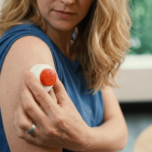 A woman placing a Tasso+ At Home Blood Test Kit on her upper arm for blood collection
